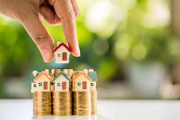 Person stacking tiny model houses on top of stacks of coins